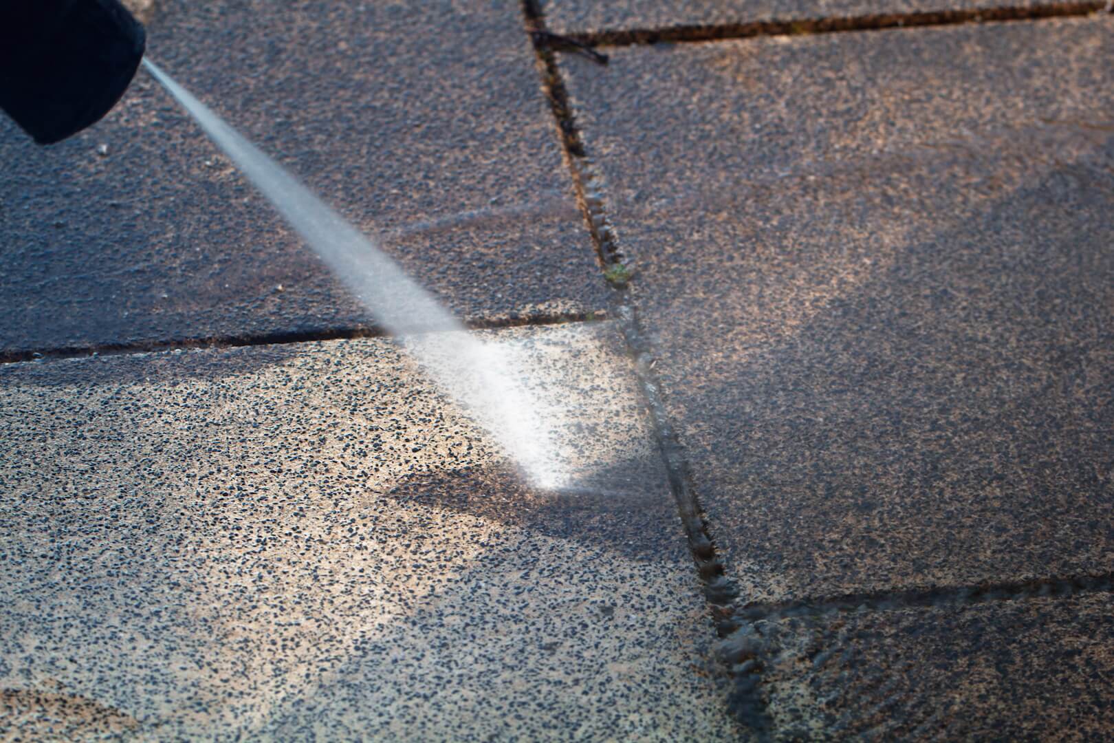Ein Wasserstrahl reinigt die verschmutzte Terasse.